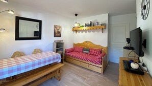 A cozy room with a bed, a bench, a wooden dresser, a TV, and a shelf with books and decorative items. - Apparemment sur les Pistes de ski Avec Piscine Risoul1850 Hautes Alpes (Risoul)
