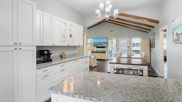 A spacious kitchen with granite countertops, white cabinetry, and a dining area with a wooden table and benches. - Updated Sunset Beach home w/ a 2-minute walk to the beach.  Parking for 5 cars. (Sunset Beach)