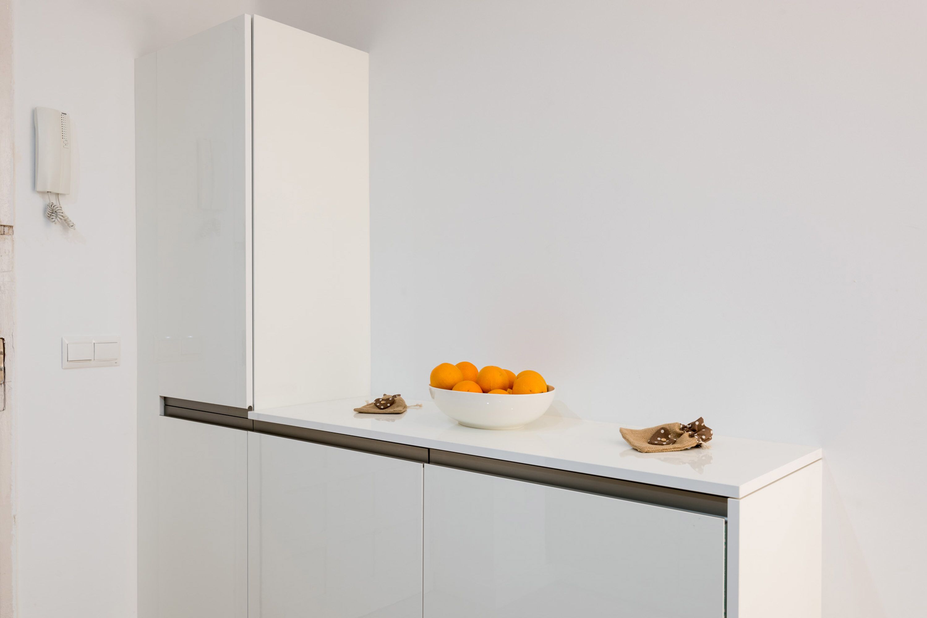 A white kitchen with a bowl of oranges on the counter.