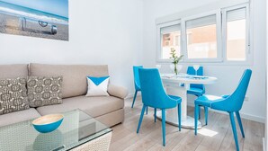 A modern living room with a beige sofa, blue chairs, a glass coffee table, and a dining table with chairs. - Solaga - Pinzon (Málaga)