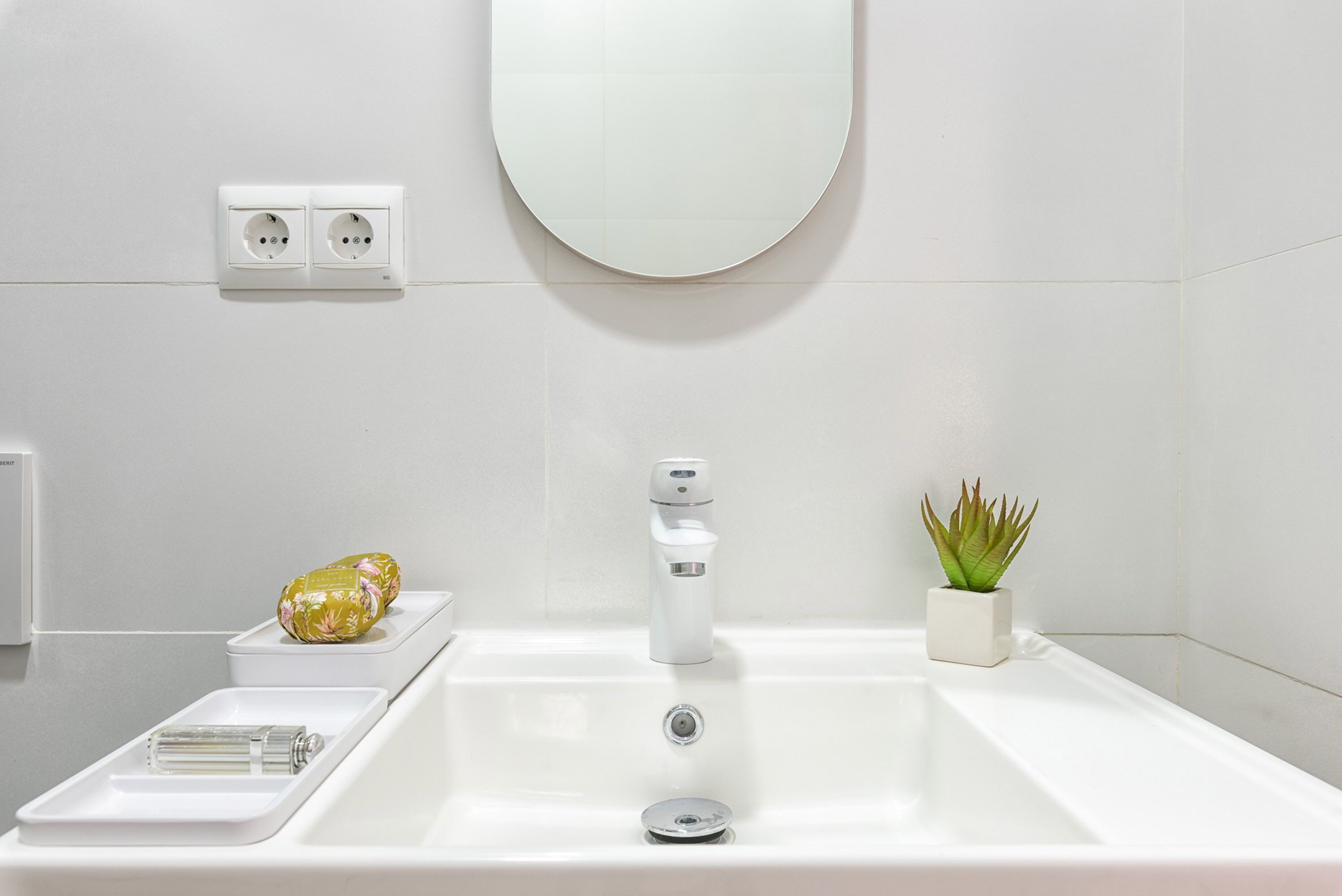 Een moderne badkamer met een wit wastafel, een spiegel, een kamerplant en een handdoekhouder.