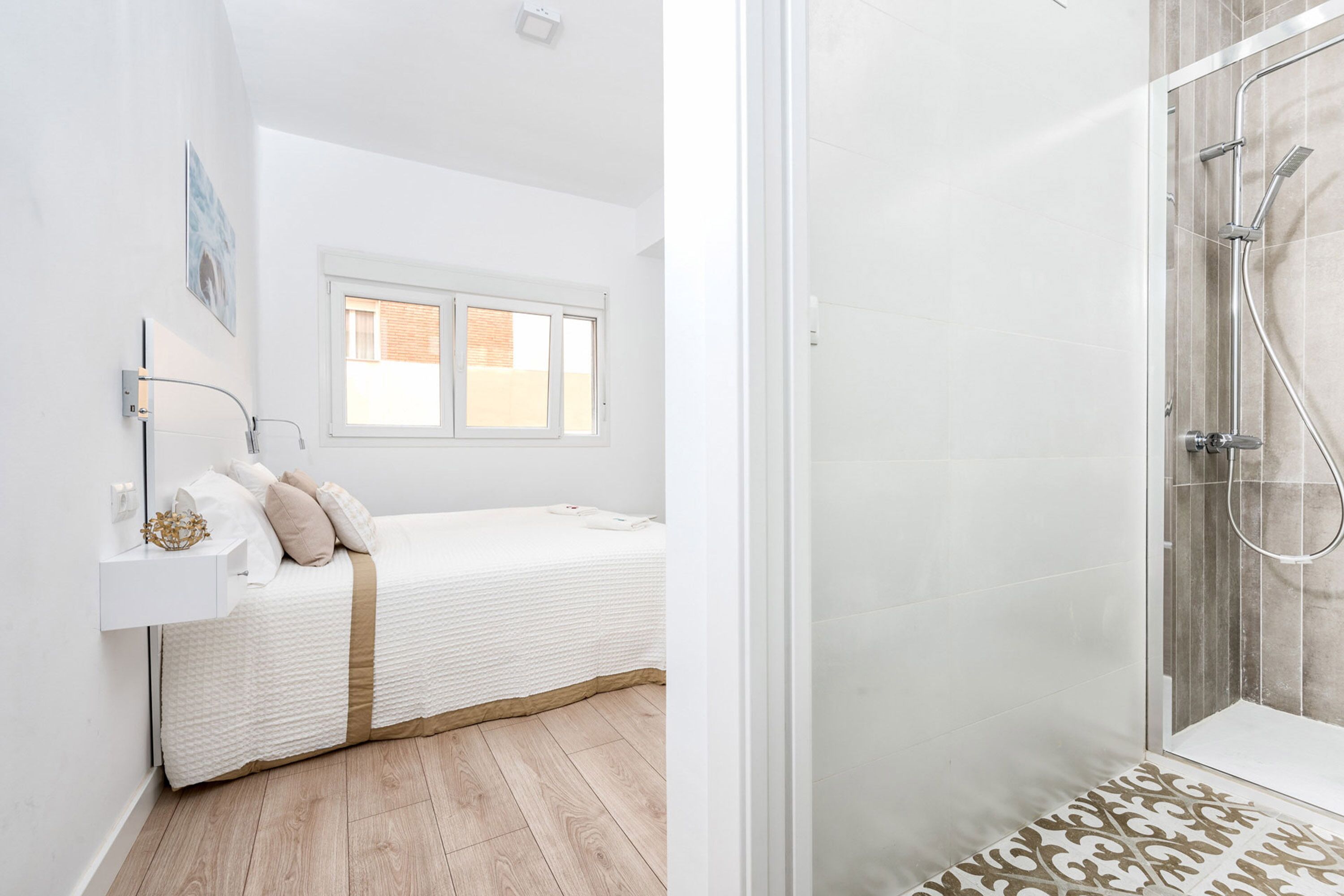 A modern bedroom with a bed, bedside table, and a shower area with a glass door.