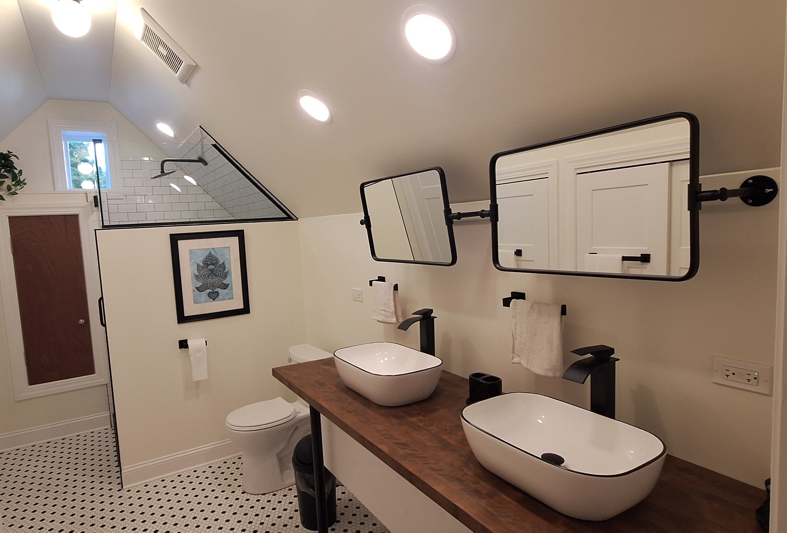 Un bagno moderno con un mobile lavabo in legno, due lavabi a posa, uno specchio grande e un water.