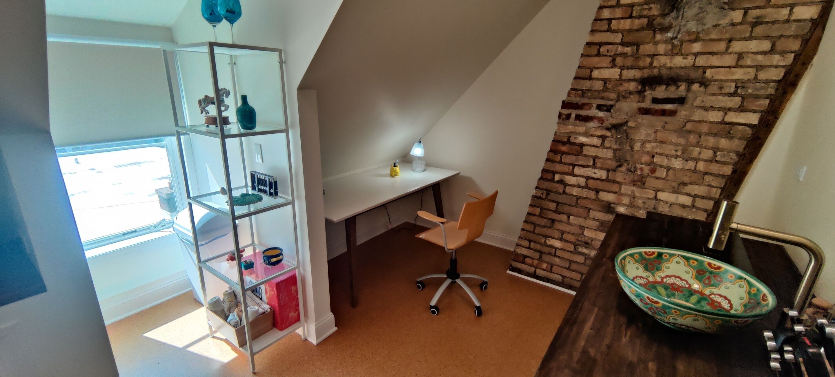 A room with a desk, chair, shelving unit, and a brick wall.