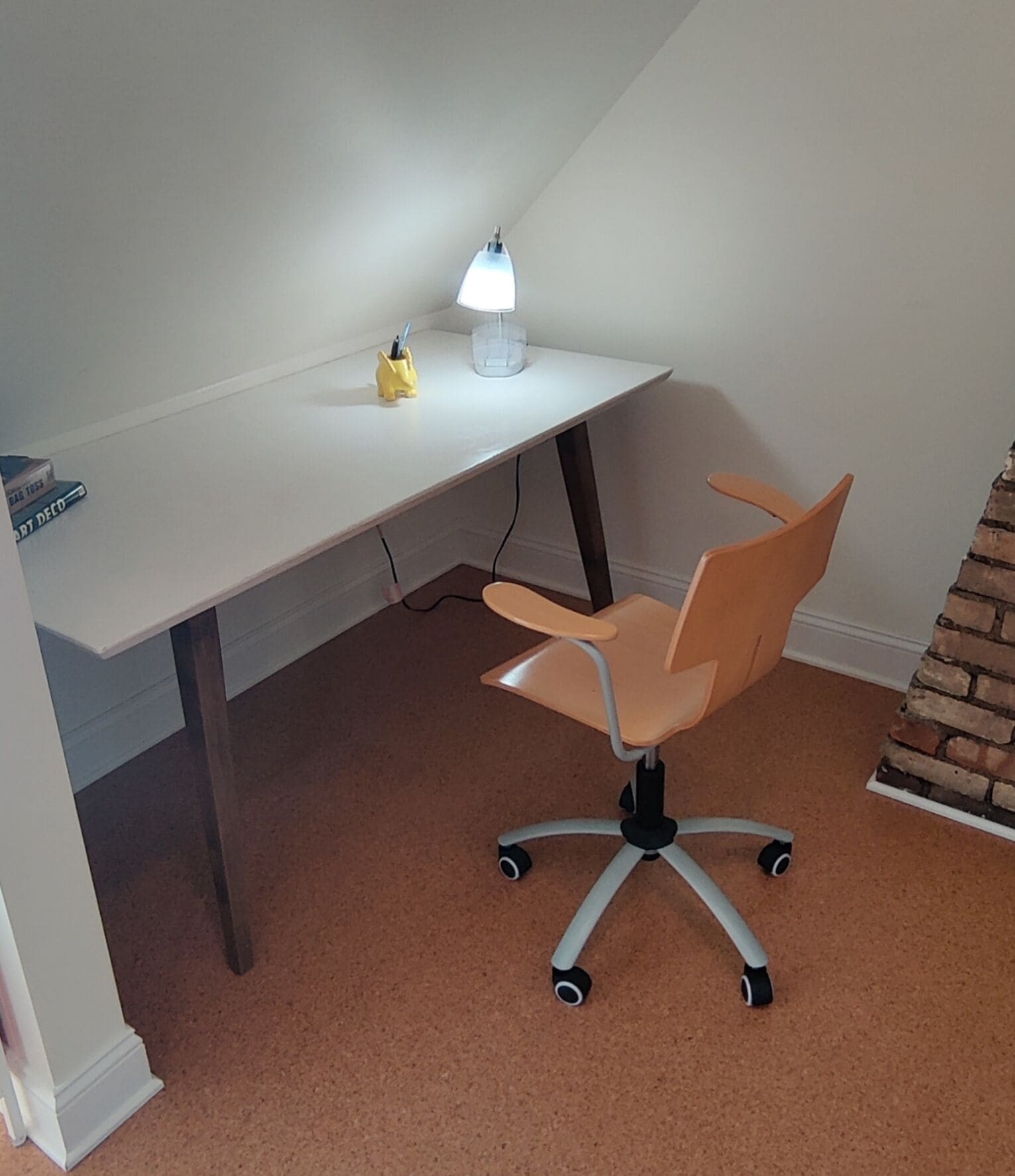 A small, angled workspace with a desk, chair, and desk lamp.