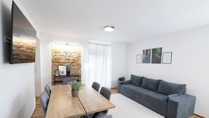 A modern living room with a wooden dining table, grey sofa, and a stone accent wall. - Modern Apartment Milo 3 room apartment for up to 6 people (Küssaberg)