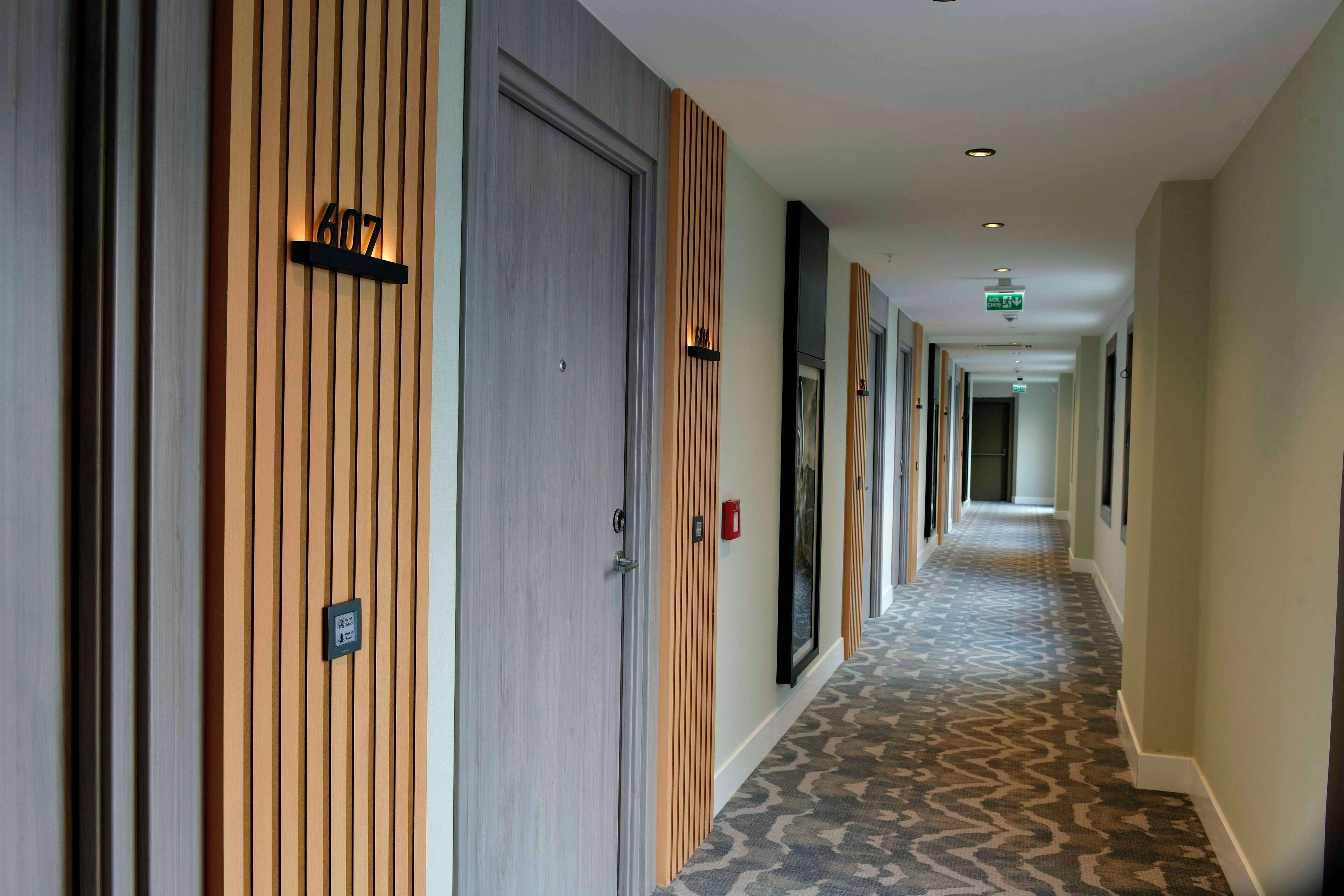 Un couloir d’hôtel avec des boiseries, des portes numérotées et un tapis à motifs.