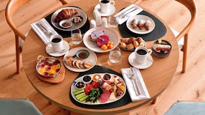 Ett runt träbord med frukosttillbehör, inklusive bakverk, frukt och drycker, omgivet av trästolar.