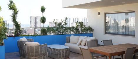 Una terraza en la azotea con mobiliario de mimbre, una mesa de madera y vistas a la ciudad.