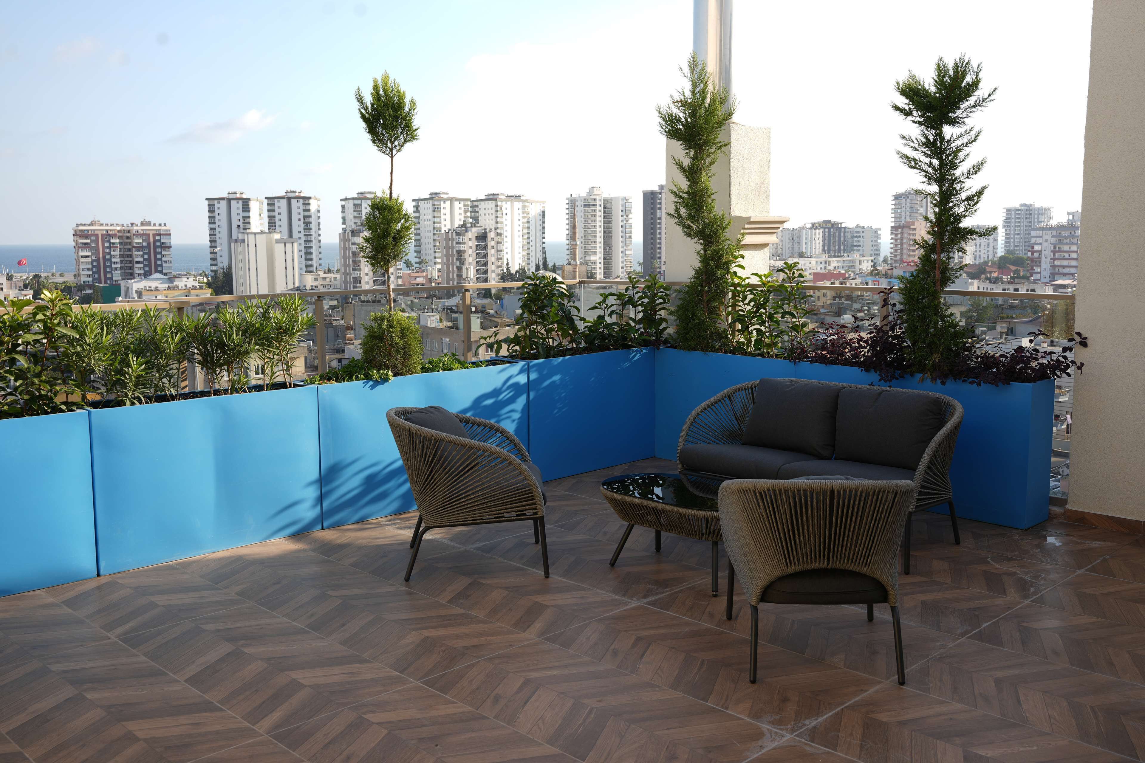 A balcony with a view of a cityscape, featuring a blue wall, wicker furniture, and potted plants.