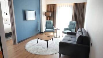 Une chambre d’hôtel moderne avec un mur d’accent bleu, un téléviseur à écran plat, un canapé, deux fauteuils, une table basse ronde et une lampe.