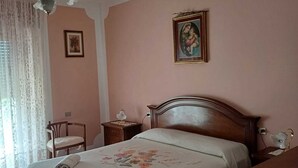 Une chambre à coucher avec un lit en bois, une table de chevet, une chaise, un ventilateur de plafond et un tableau encadré au mur.