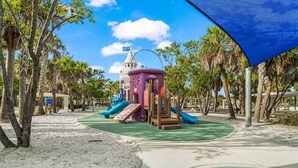 Un'area giochi con scivoli e strutture per arrampicarsi, circondata da palme e un cielo sereno.