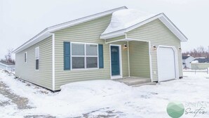Een gelijkvloers huis met een veranda, een garage en een met sneeuw bedekte dak.