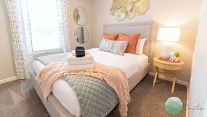 Een slaapkamer met een bed, nachtkastje, lamp en decoratieve wandkunst.
