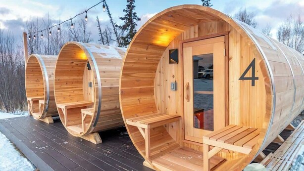 Drie houten blokhutten, waarvan er één het nummer '4' heeft, verbonden door een houten terras.
