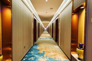 A hotel corridor with doors on both sides, a patterned carpet, and a vase on a shelf. - Friendship Peak Hotel (Burqin)