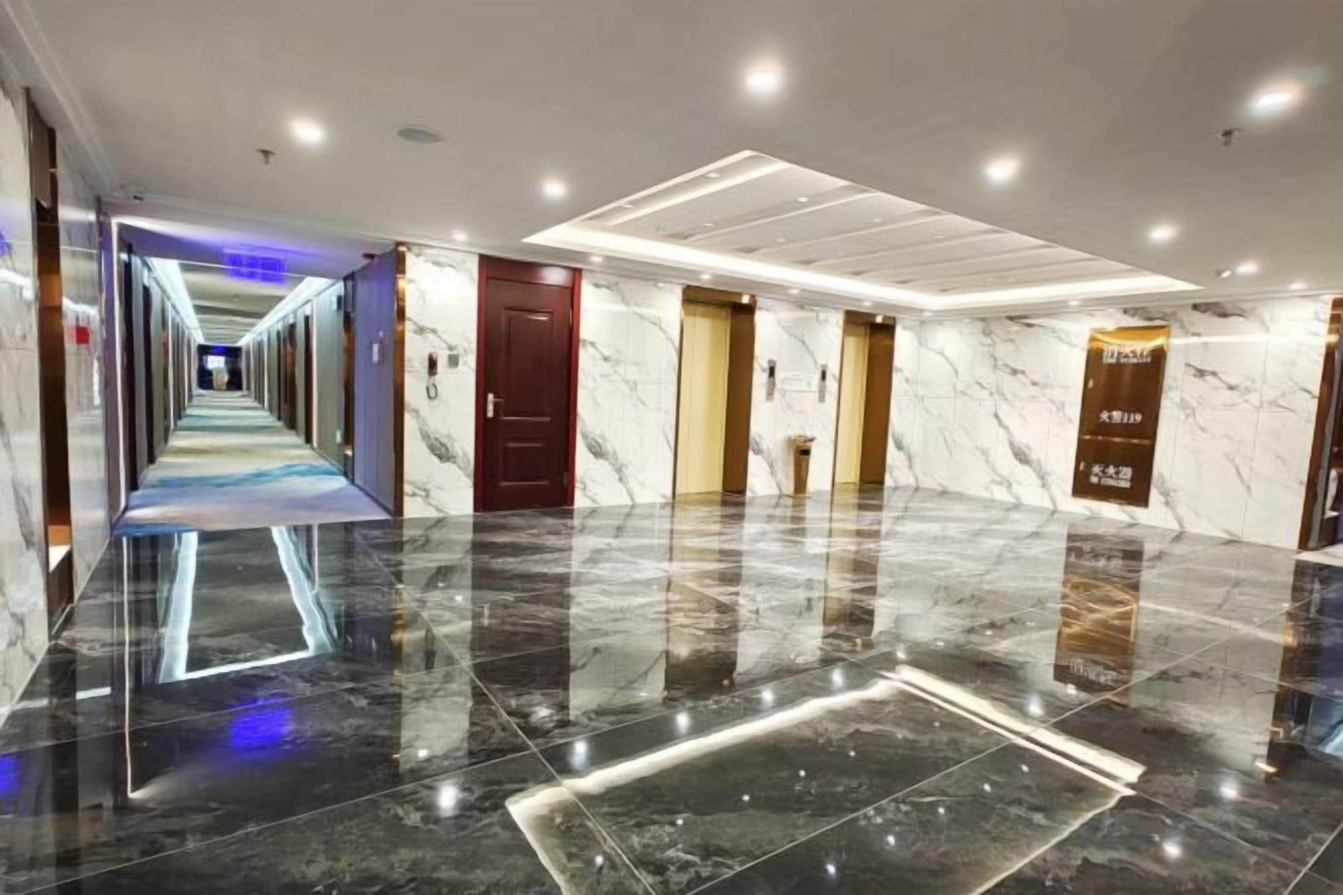 A hotel corridor with a reflective floor, doors, and a hallway leading to another area.