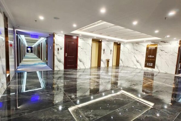 A hotel corridor with a reflective floor, doors, and a hallway leading to another area. - Friendship Peak Hotel (Burqin)
