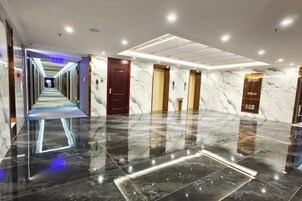 Pasillo de hotel con piso reflectante, puertas y un corredor que conduce a otra área.