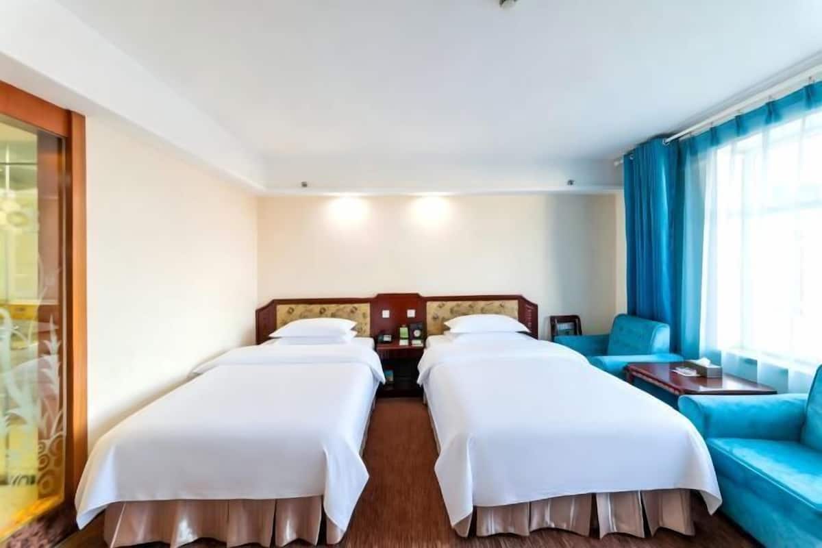 A hotel room with two beds, a sofa, a nightstand, and a window with curtains.