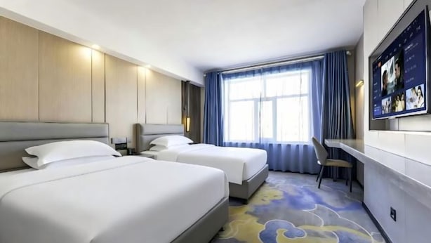 A hotel room with two beds, a desk, a chair, a large window with curtains, and a TV mounted on the wall. - Friendship Peak Hotel (Burqin)