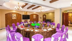 A conference room with round tables, purple chairs, and a wooden ceiling. - Friendship Peak Hotel (Burqin)