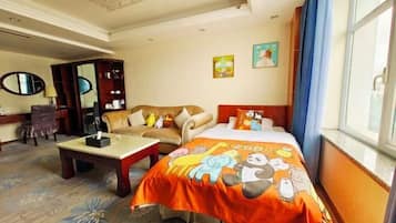 A hotel room with a bed, a sofa, a desk, and a chair. There are paintings on the wall and a window with curtains.