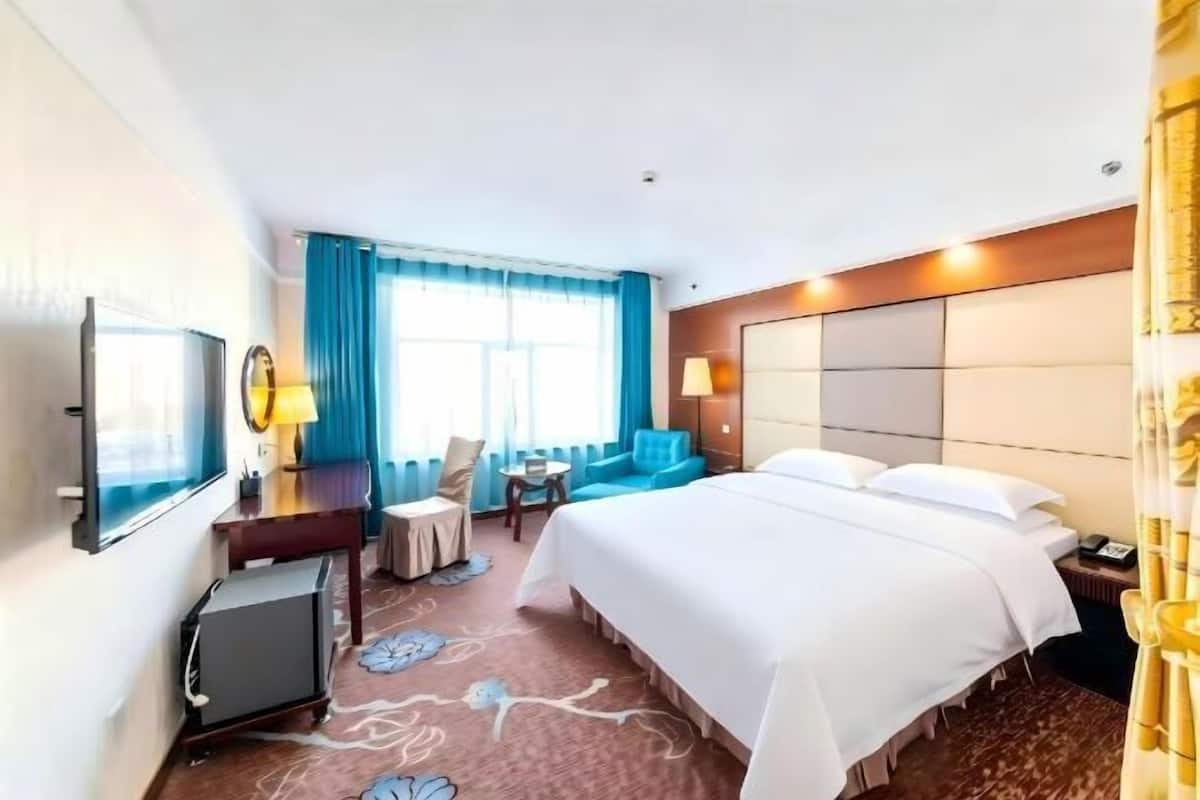 A hotel room with a bed, a desk, a chair, a TV, and a window with curtains.