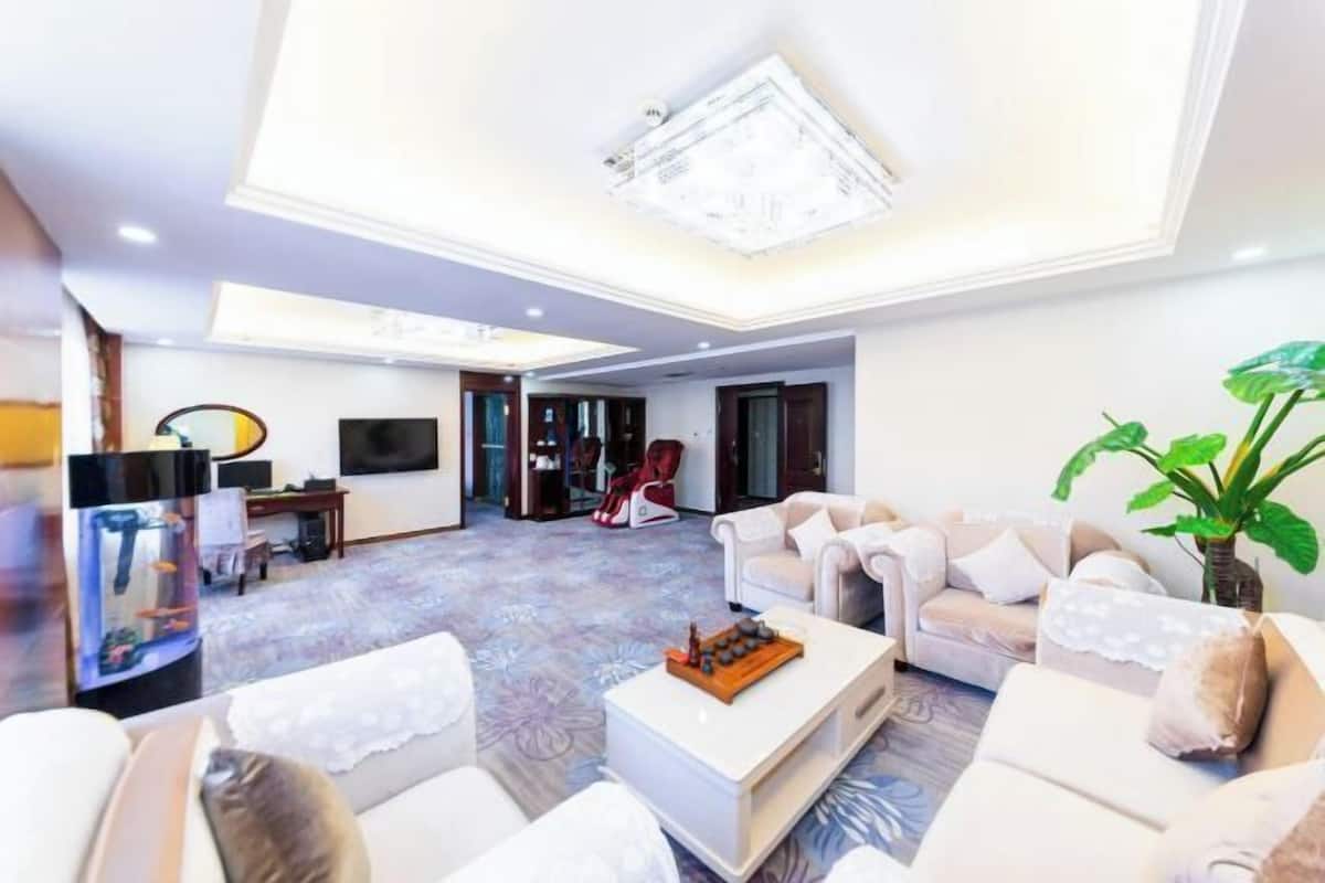 A spacious living room with a high ceiling, a chandelier, a large plant, and a television.