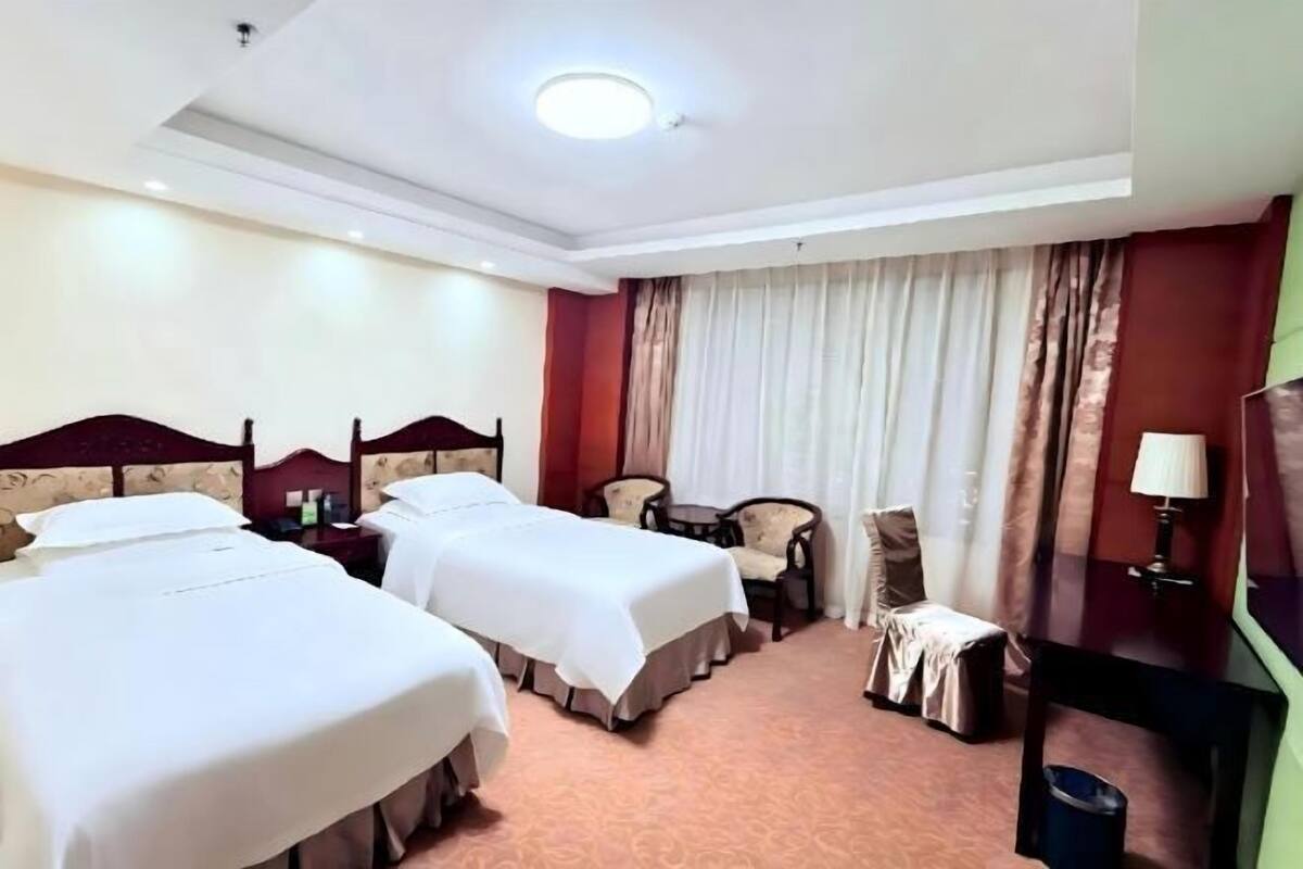 A hotel room with two beds, a desk, a chair, a TV, and a window with curtains.
