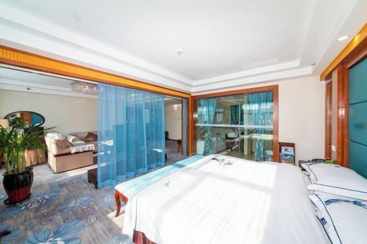 A hotel room with a large bed, a seating area with a sofa and chairs, and a glass partition.