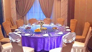 A round table with a purple tablecloth, surrounded by white chairs with silver bows. - Friendship Peak Hotel (Burqin)