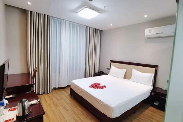 A hotel room with a bed, curtains, an air conditioner, a desk with a telephone, and a television. - Century Business Hotel (Meitan)