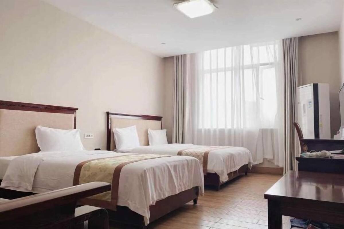 A hotel room with two beds, a wooden headboard, a flat-screen TV, and a large window with curtains.