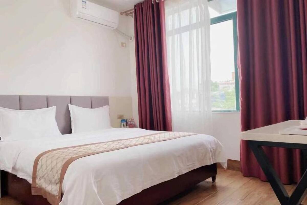 A hotel room with a bed, a table, and a window with curtains.