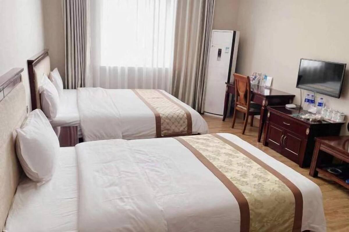 A hotel room with two beds, a desk, a chair, a television, and a refrigerator.
