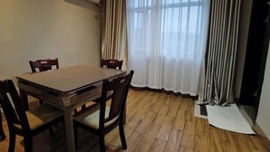 A dining area with a wooden table and chairs, a window with sheer curtains, and an air conditioning unit on the wall.