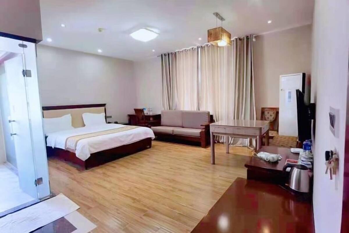 A hotel room with a bed, a sofa, a small table, a TV, and a door.