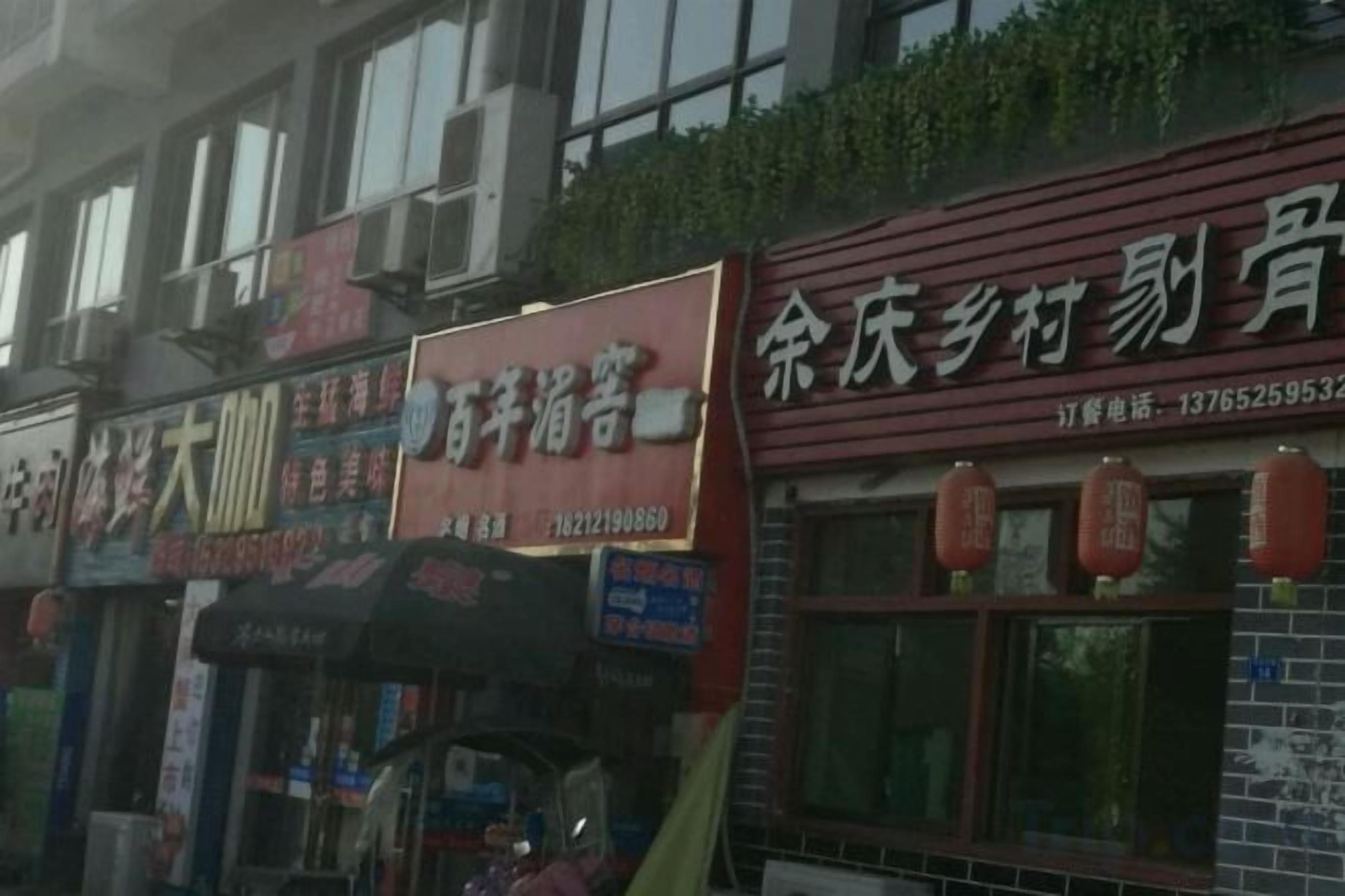 A row of storefronts with signage, including a restaurant and a shop with a red awning.