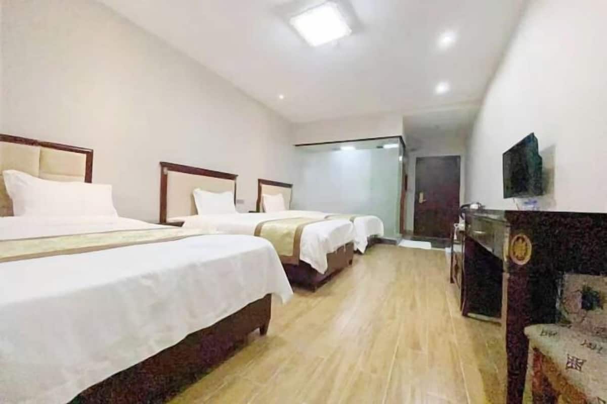 A hotel room with three beds, a flat-screen TV, and a wooden floor.