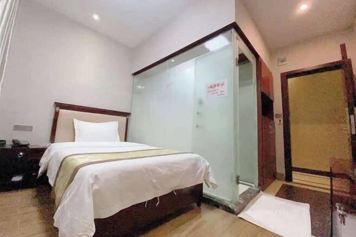 A hotel room with a bed, a nightstand, a glass partition, and a door.