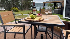 Un área de comedor al aire libre con una mesa dispuesta para dos personas, que incluye una botella de vino, un cuenco de uvas y queso.