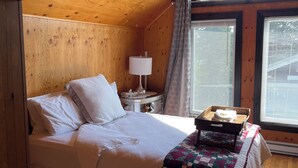 Un dormitorio acogedor tipo cabaña de madera, con una cama, una mesita de noche, una lámpara y una ventana con cortinas.
