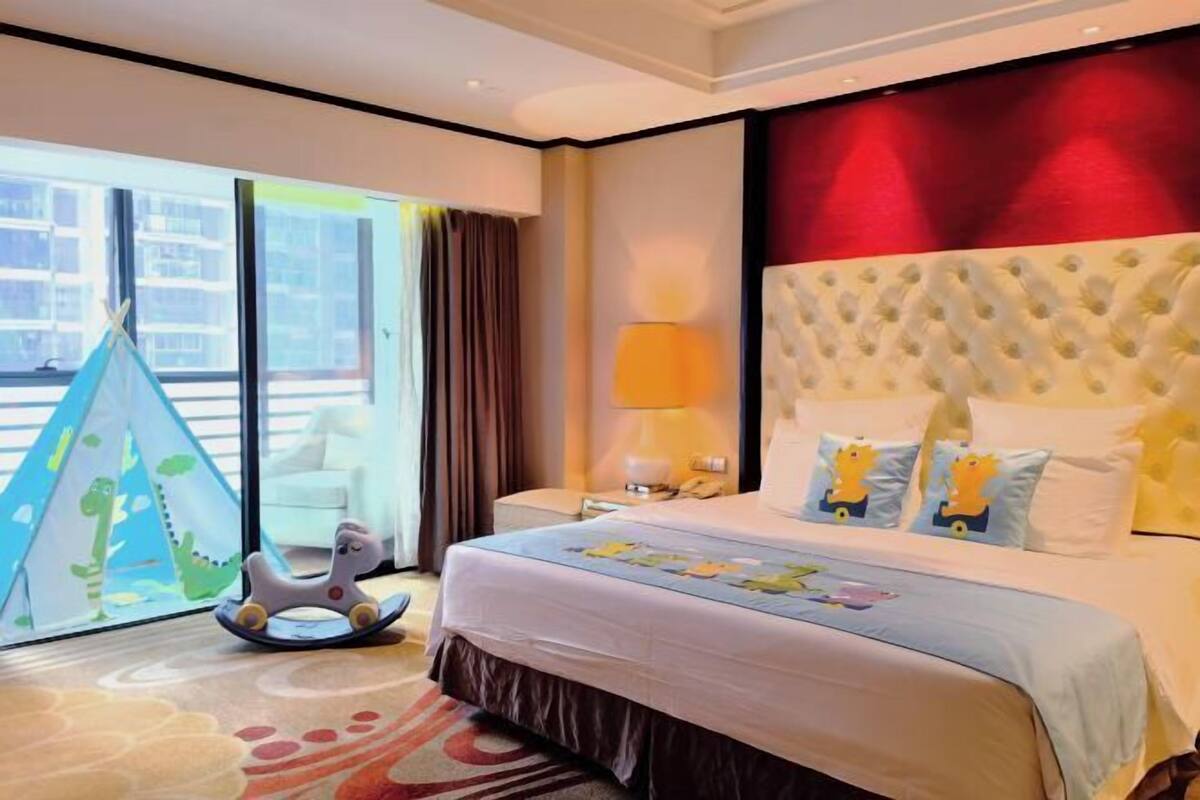 Habitación de hotel con una cama grande, vistas a través de una puerta corredera, una lámpara y un osito de peluche sobre la cama.