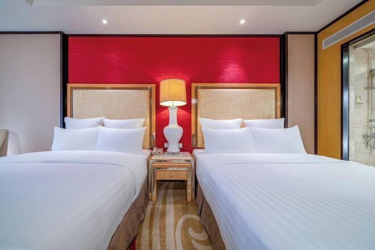 Habitación de hotel con dos camas, una pared de acento roja y una lámpara entre ellas.