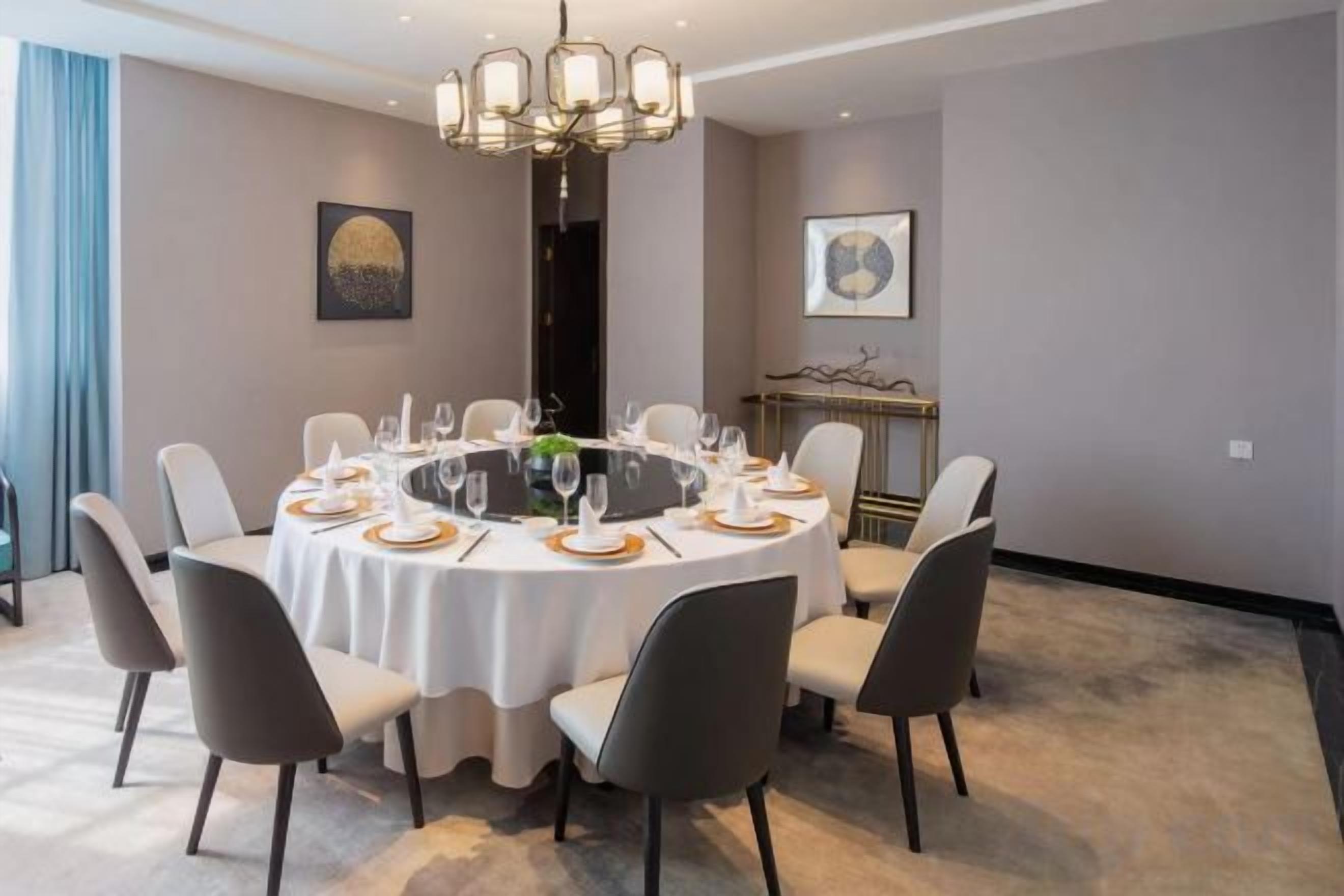 A round dining table with chairs, a chandelier, and a fireplace in the background.