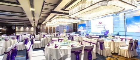 A banquet hall with round tables, chairs, and a chandelier.