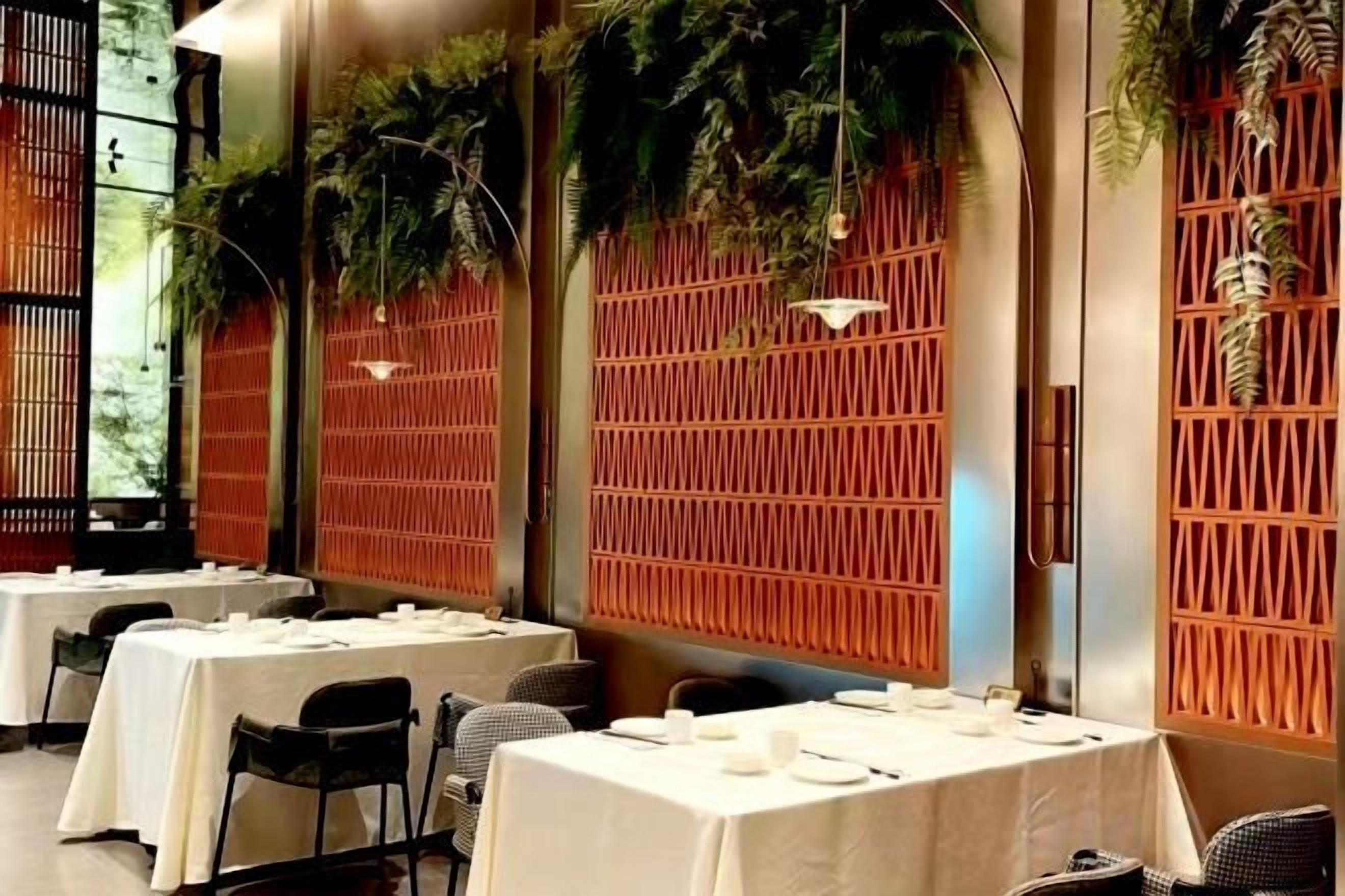 A restaurant with tables set for dining, a bamboo partition wall, and hanging greenery.