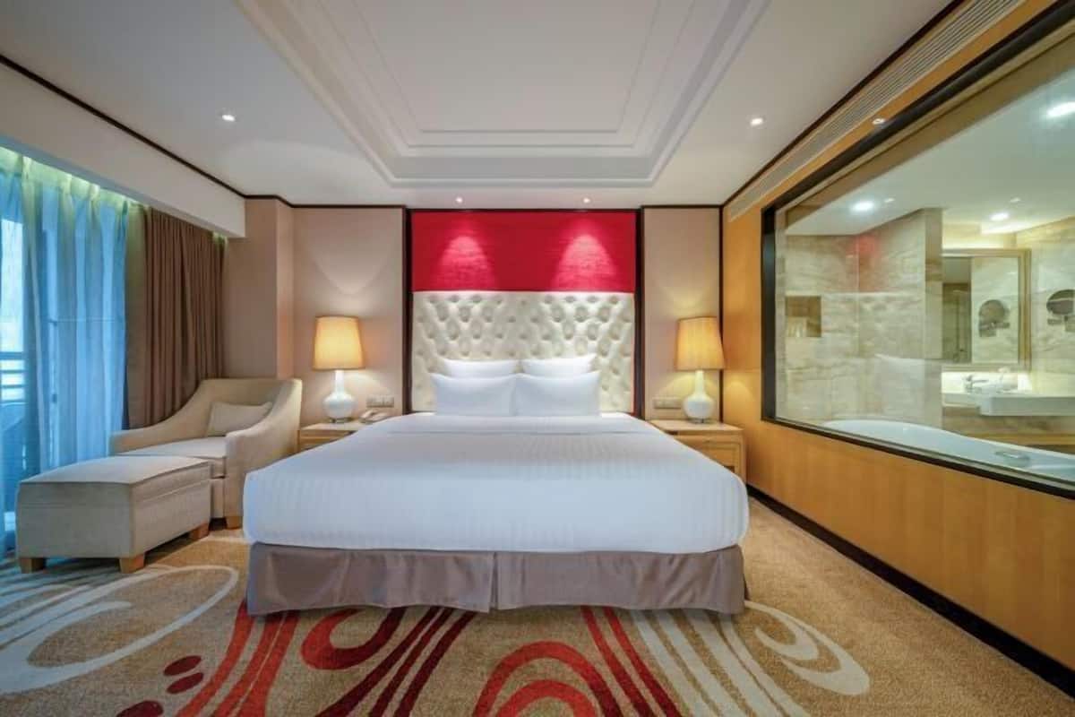 Habitación de hotel con una cama grande, dos lámparas de noche, una silla, un espejo amplio y vistas al baño.